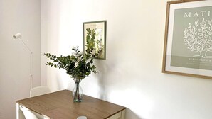 Ein Essbereich mit Holztisch, weißen Stühlen, einer Vase mit Blumen und gerahmten Pflanzenbildern an der Wand.