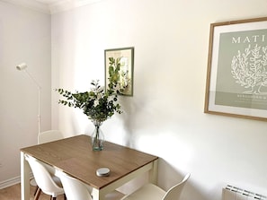 A dining area with a wooden table, white chairs, a vase with flowers, and framed botanical prints on the wall. - Luxury By The Coast 7 (Galway)