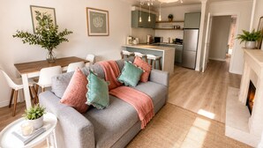 Ein modernes Wohnzimmer mit einem grauen Sofa, einem Esstisch und einer Küche im Hintergrund.