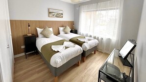 Ein Hotelzimmer mit zwei Betten, einem Nachttisch, einer Lampe, einem Fenster mit Vorhängen und einem Bild an der Wand.