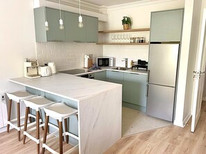 A modern kitchen with a central island, bar stools, a microwave, a refrigerator, and hanging pendant lights. - Luxury By The Coast 7 (Galway)