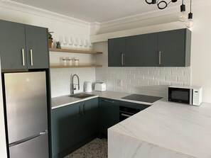 A modern kitchen with dark cabinets, a stainless steel refrigerator, a white countertop, a microwave, and a sink.