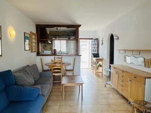 Un salon avec un canapé, une table à manger avec des chaises, un coin cuisine avec une fenêtre et un meuble en bois.