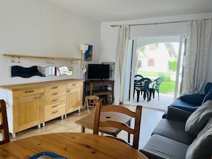 A room with a wooden dining table, a sofa, a TV, and a sliding glass door leading to an outdoor area with chairs. - Apartment in Denia - Perfect for Your Vacation (Denia)