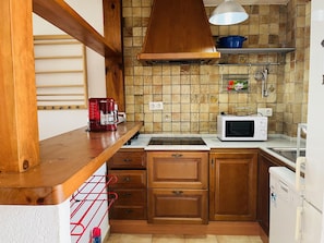 A compact kitchen with wooden cabinets, a built-in microwave, a coffee maker, and a hanging rack. - Apartment in Denia - Perfect for Your Vacation (Denia)