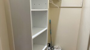 Un placard de rangement avec des étagères ouvertes, une serpillière et une poubelle.