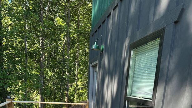 Une terrasse en bois avec une table ronde et des chaises en osier, une fenêtre avec des stores et un mur végétal.