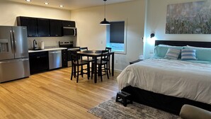 Une chambre moderne comprenant un lit, une petite table et des chaises, un coin cuisine avec des appareils électroménagers et un ventilateur de plafond.