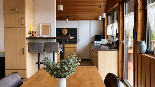 Eine moderne Küche mit Holzausstattung, einem Esstisch mit Stühlen und einem großen Fenster mit Vorhängen.