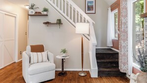 A staircase with a white railing, a light floor lamp, a chair with a brown throw, and a small table with a plant.