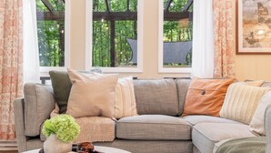 A living room with a grey sofa, a round coffee table, and a window with a view of trees.