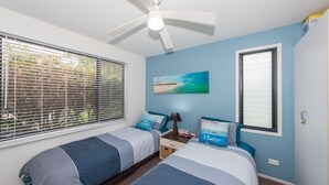 A bedroom with two beds, a ceiling fan, a beach-themed painting, and a window with blinds. - Sandy Shores, Serenity Resort (Diamond Beach)