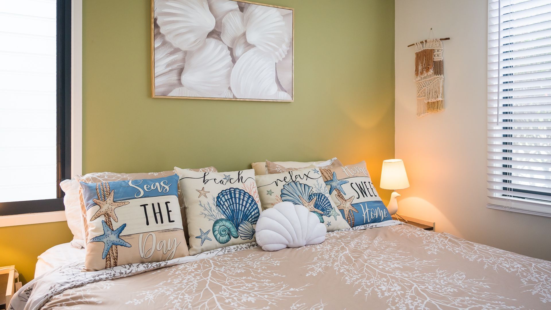 A bedroom with a bed, pillows with nautical designs, a wall art piece, and a bedside lamp.