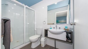 A modern bathroom with a glass-enclosed shower, a white toilet, and a sink with a mirror above. - Sandy Shores, Serenity Resort (Diamond Beach)