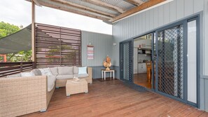 A covered outdoor seating area with a sofa and a table, a kitchen visible through a sliding glass door, and a sign with a message. - Sandy Shores, Serenity Resort (Diamond Beach)