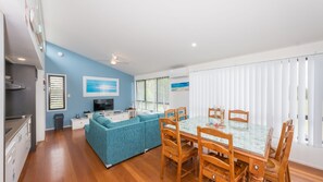 A modern living space with a dining area, kitchen, and a large window with blinds. - Sandy Shores, Serenity Resort (Diamond Beach)