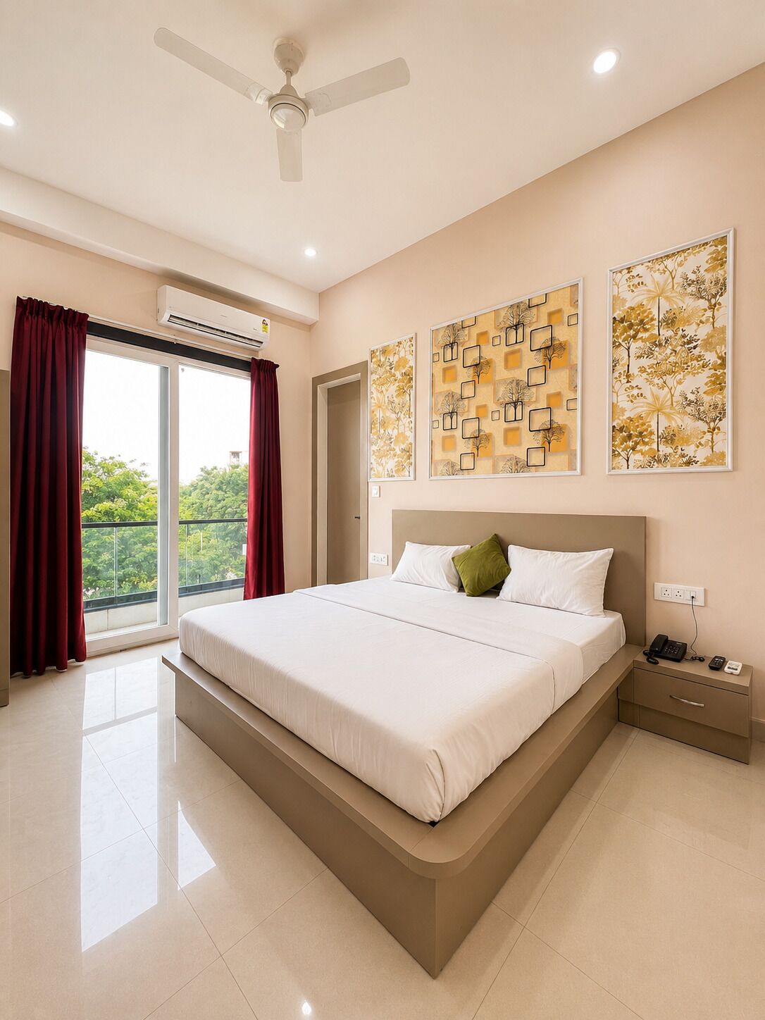 Una habitación de hotel moderna con una cama grande, un ventilador de techo, un equipo de aire acondicionado, una mesita de noche con un teléfono y obras de arte en las paredes.