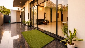 A modern building with large glass windows, a green artificial turf area, and potted plants. -  Hotel Blue Fern - Near India Expo Center & Mart, Greater Noida (Greater Noida)
