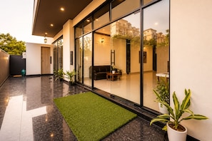 A modern building with large glass windows, a green artificial turf area, and potted plants.