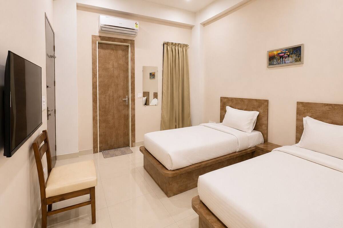 Habitación de hotel con dos camas, un televisor, una puerta y un ventilador de techo.