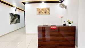 A reception desk with a 'RECEPTION' sign, a wall-mounted fan, and a framed artwork above it. -  Hotel Blue Fern - Near India Expo Center & Mart, Greater Noida (Greater Noida)