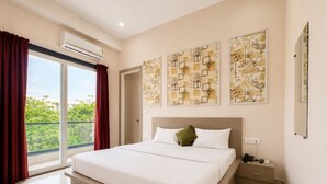 A modern bedroom with a large bed, a nightstand, a mirror, and artwork on the walls. -  Hotel Blue Fern - Near India Expo Center & Mart, Greater Noida (Greater Noida)