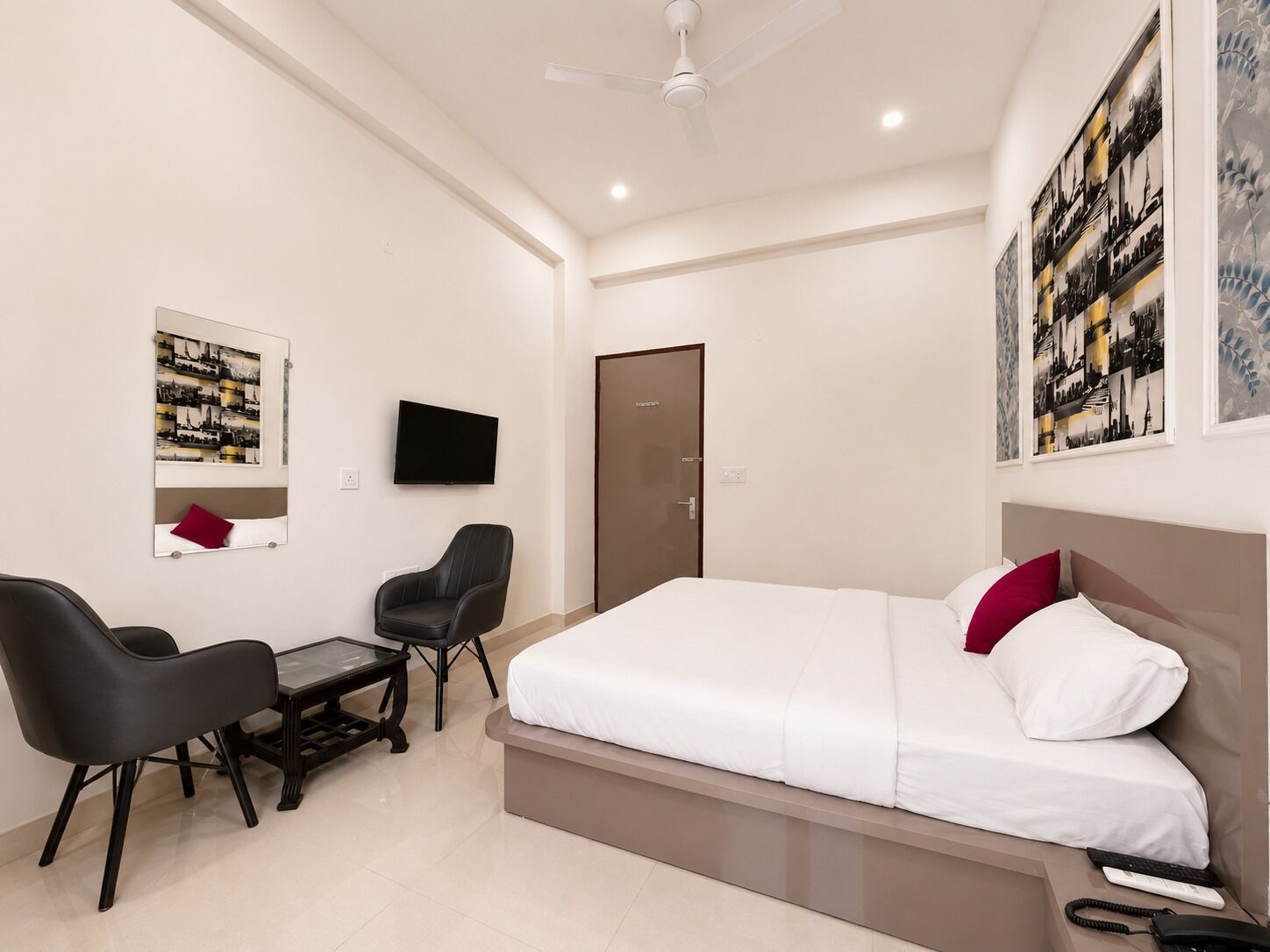 Quarto de hotel com cama, escrivaninha, cadeira, televisão e porta.