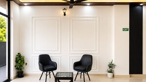 A lobby with two black chairs, a glass-top table, a ceiling fan, and an exit sign. -  Hotel Blue Fern - Near India Expo Center & Mart, Greater Noida (Greater Noida)