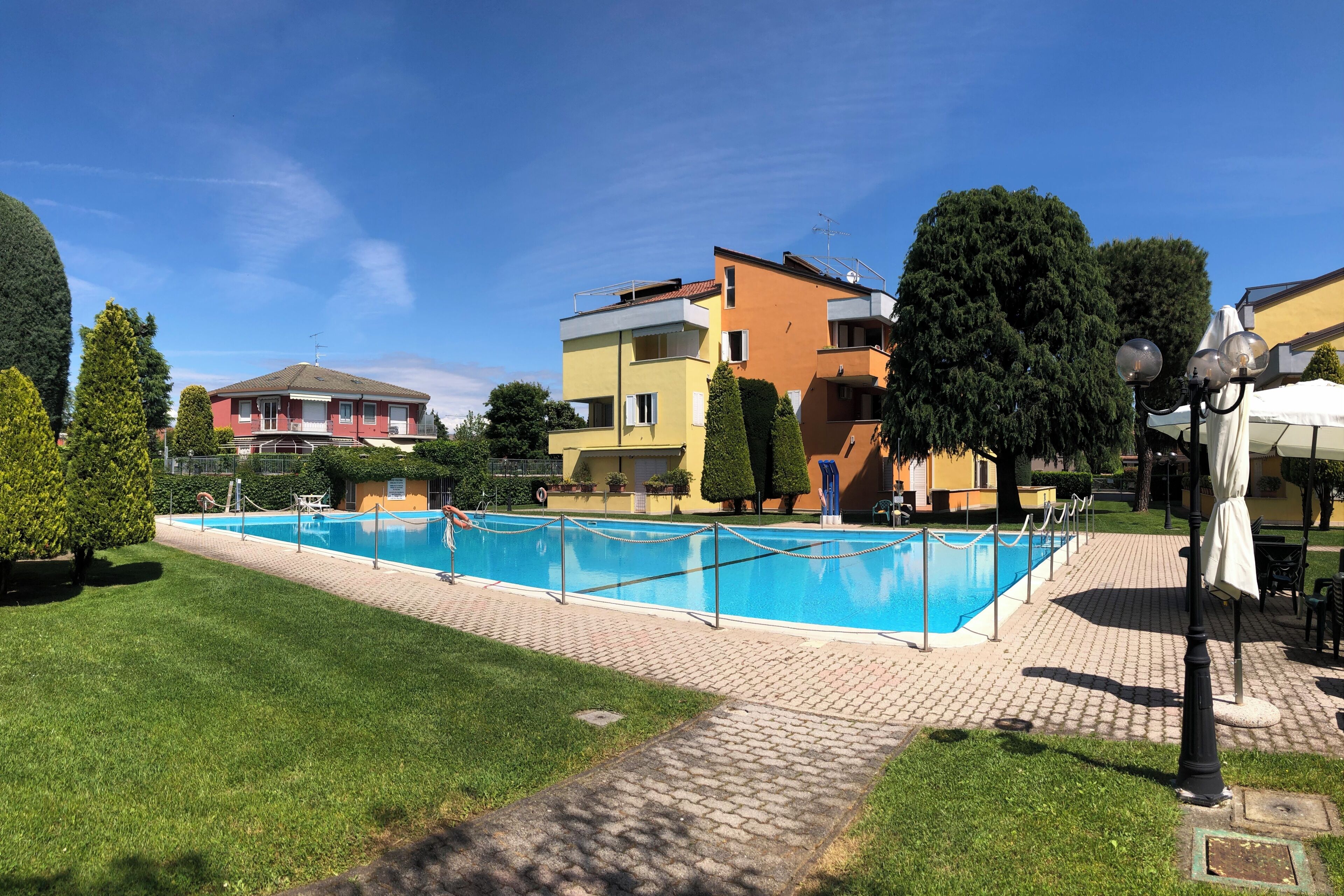 A swimming pool with a fence, surrounded by a paved walkway, and adjacent to multi-story residential buildings.