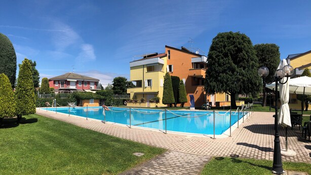 Una piscina con valla, rodeada de un sendero pavimentado, junto a edificios residenciales de varios pisos.