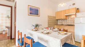 Un comedor con una mesa dispuesta para cuatro, una cocina con armarios de madera, un refrigerador y un salpicadero de azulejos.