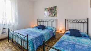 Una habitación con dos camas, una ventana con cortinas translúcidas, un cuadro abstracto en la pared y un suelo estampado.