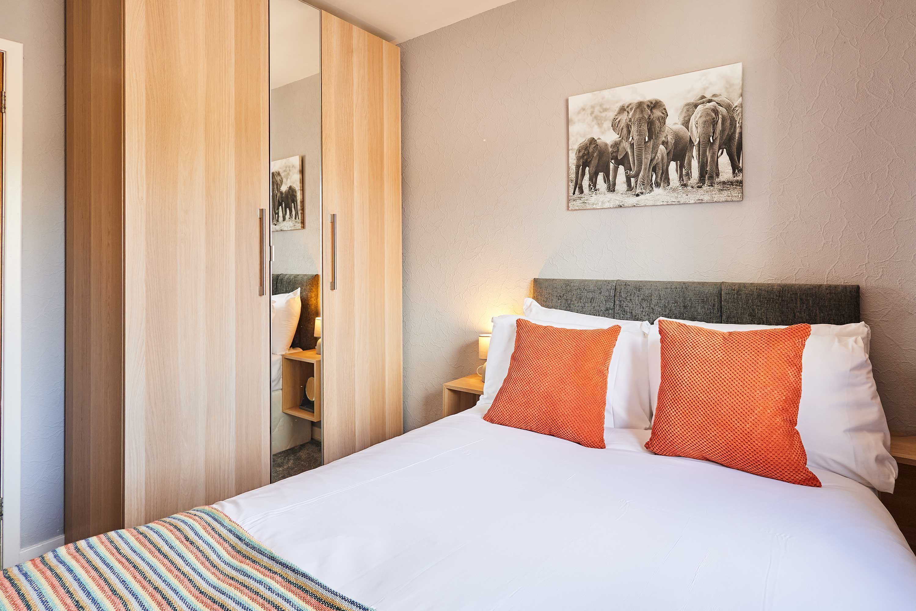 Ein Hotelzimmer mit einem Bett, einem Nachttisch, einem an der Wand befestigten Bild von Elefanten und einem Holzschrank.