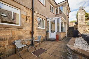 A stone building with a patio area, two chairs, a table, and a grill. - Host Stay - The Mews (Morpeth)