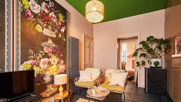 A living room with a flat-screen TV, wicker furniture, a decorative wall with floral artwork, and a green ceiling. - Host Stay - Little Marjorelle (Berwick-upon-Tweed)