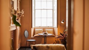 A cozy room with a window seat, a small table, a mirror, and a potted plant. - Host Stay - Little Marjorelle (Berwick-upon-Tweed)