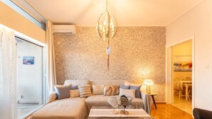 Ein gemütliches Wohnzimmer mit einer Couch, einem Glastisch, einer Deckenleuchte und einem Essbereich, der durch eine offene Tür sichtbar ist.