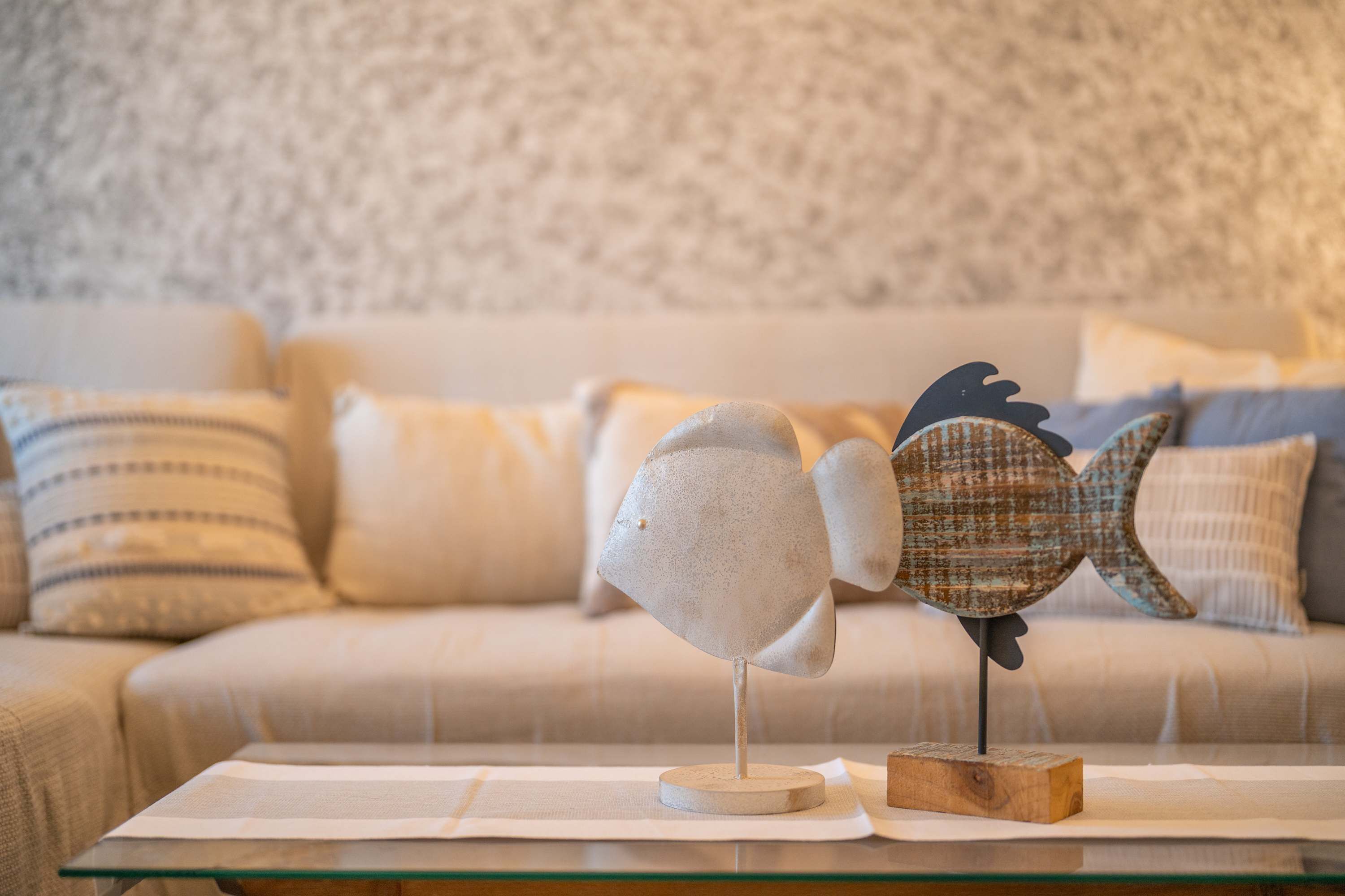 A room with a glass coffee table, a decorative fish sculpture, and a patterned sofa.