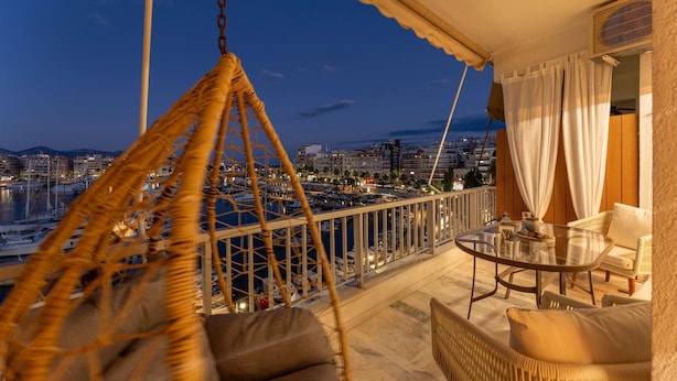 Ein Balkon mit Korbmöbeln, einem Glastisch und Blick auf einen Yachthafen und die Skyline der Stadt.