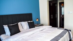 A neatly made bed with white and gray bedding, a black headboard, and a bedside lamp. - Yogi 1BR Business Bay Gym Pool Parking (Dubai)
