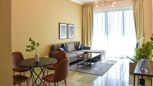 A modern living room with a sofa, coffee table, and chairs. There are two framed pictures on the wall and a plant on the table. - Yogi 1BR Business Bay Gym Pool Parking (Dubai)