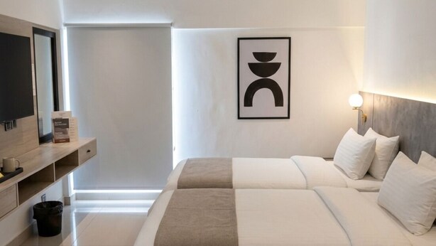 A modern bedroom with a large bed, a bedside table, a wall-mounted TV, and a framed artwork. - Hamsun Clifton Apartment 3 Bedroom (Karachi)