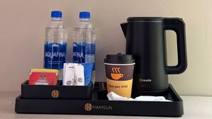 A tray with two Aquafina water bottles, a coffee cup, a creamer, a box of Tafel Danedar, and a black coffee maker. - Hamsun Clifton Apartment 3 Bedroom (Karachi)