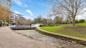 A paved walkway, a fountain, and a grassy area with trees. - Your East Perth Haven awaits! Walk to Optus Stadium, Crown Perth and the CBD. Enjoy iconic Swan River walks, vibrant Claisebrook Cove for coffee and dining and super easy city access with the free CAT bus (20mins). (East Perth)