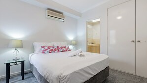 A hotel room with a bed, bedside lamps, a mirror, a wardrobe, and an air conditioning unit. - Your East Perth Haven awaits! Walk to Optus Stadium, Crown Perth and the CBD. Enjoy iconic Swan River walks, vibrant Claisebrook Cove for coffee and dining and super easy city access with the free CAT bus (20mins). (East Perth)
