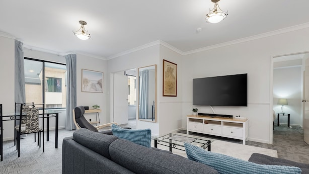 A modern living room with a sofa, TV, and dining area. - Your East Perth Haven awaits! Walk to Optus Stadium, Crown Perth and the CBD. Enjoy iconic Swan River walks, vibrant Claisebrook Cove for coffee and dining and super easy city access with the free CAT bus (20mins). (East Perth)