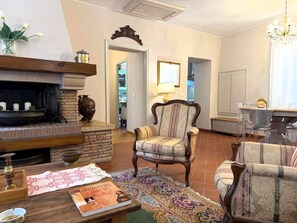 A living room with a fireplace, a patterned armchair, a table with a book, and a rug. - Beautiful apartment for 6 guests with A/C, WIFI and panoramic view (Cortona)
