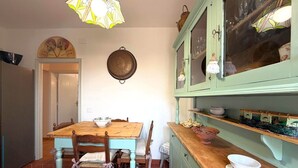 Uma área de jantar com mesa e cadeiras de madeira, luminária pendente e armário com portas de vidro.