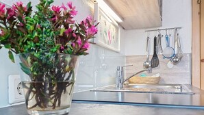 Een keuken met een glazen vaas vol roze bloemen, een roestvrijstalen spoelbak en hangend keukengerei.