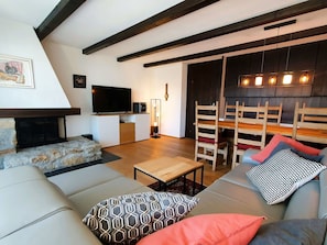 Ein Wohnzimmer mit Sofa, Couchtisch, Fernseher, Kamin und Essbereich mit Stühlen und Tisch.